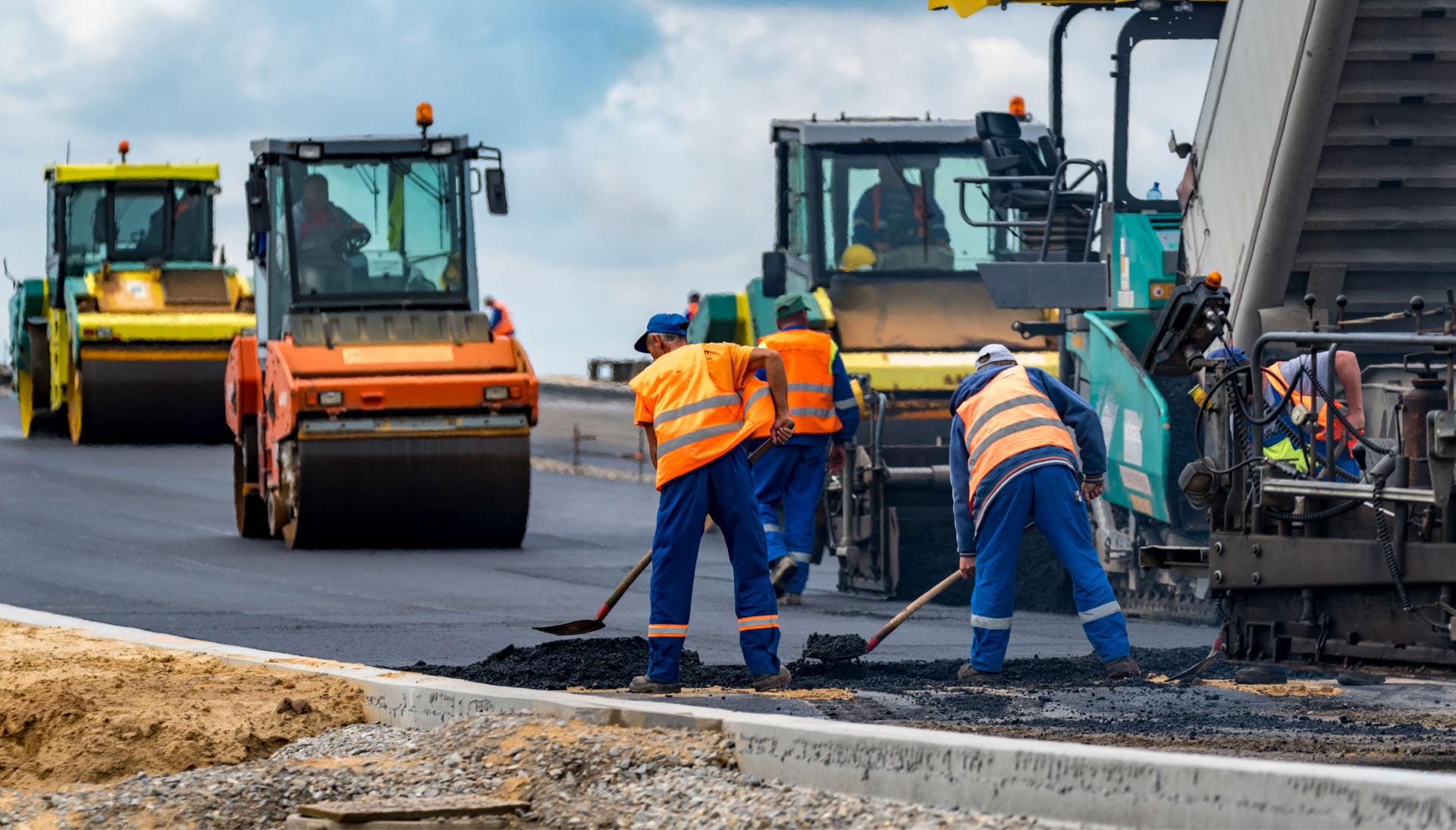 A group of construction workers wearing hard hats and reflective vests, operating heavy machinery and laying down asphalt on a newly excavated road in Peoria, showcasing the intricate process of building a sturdy and smooth surface.